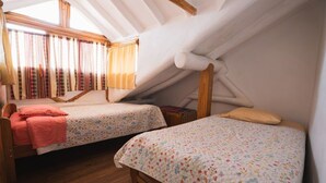 Un dormitorio con dos camas, cabeceros de madera, una ventana con cortinas y techo inclinado.