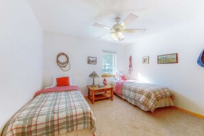Une chambre avec deux lits, un ventilateur de plafond, une fenêtre et des tableaux accrochés au mur.
