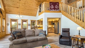 A spacious living area with a wooden ceiling, a sofa, a coffee table, a leather chair, and a staircase leading to an upper level. - The Bear Chalet - Hot Tub, Game Room, Mtn Views (Angel Fire)