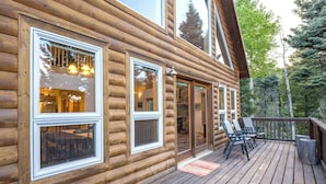 A log cabin with large windows, a deck with outdoor seating, and a view of the surrounding forest. - The Bear Chalet - Hot Tub, Game Room, Mtn Views (Angel Fire)