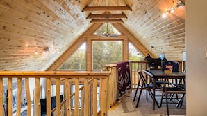 A wooden interior with a sloped ceiling, a table with chairs, and a window. - The Bear Chalet - Hot Tub, Game Room, Mtn Views (Angel Fire)