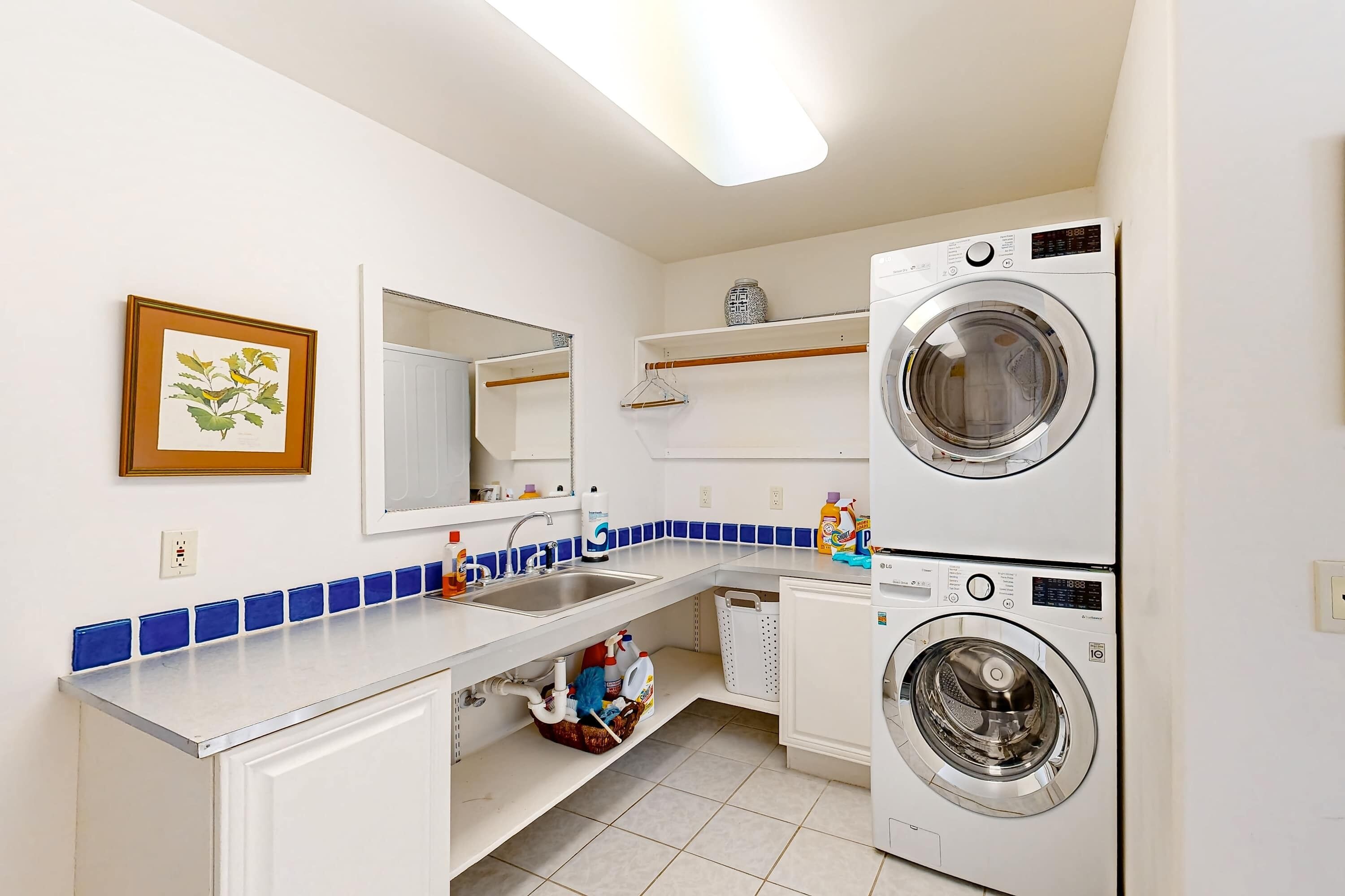 Une buanderie équipée d’un lave-linge, d’un évier, d’un miroir et d’un mur recouvert de carreaux.