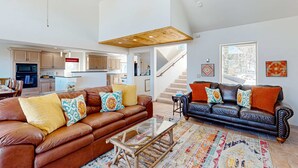A spacious living area with two sofas, a coffee table, and a kitchen in the background. - Southwest Heaven - Sweeping Views, Hot Tub & Deck (Angel Fire)