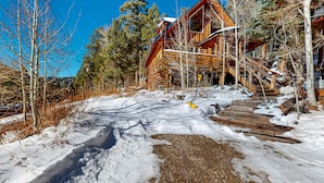 A log cabin with a wooden exterior, a staircase leading to a deck, and a snowy ground. - Ridgerunner Cabin - Ski Retreat with Hot Tub (Taos Ski Valley)