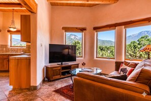 A living room with a TV, sofa, and windows offering mountain views.
