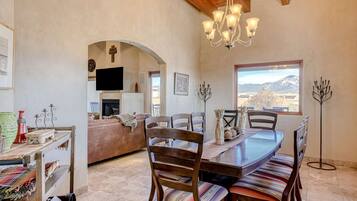 A dining area with a wooden table and chairs, a chandelier, and a view of mountains through a window.