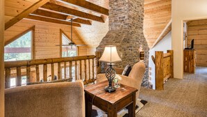 Interior acogedor de una cabaña con chimenea de piedra, vigas de madera y un balcón con barandilla.