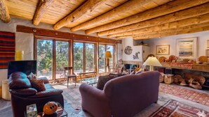 Un vaste espace de vie doté d’un plafond en bois, de grandes fenêtres, d’une cheminée et d’un téléviseur.