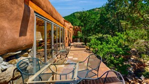 Une terrasse avec des sièges extérieurs, une entrée avec une porte vitrée et une vue sur une colline boisée.