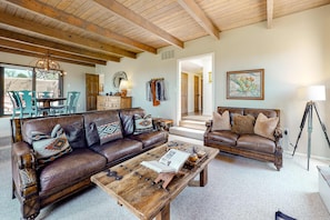 Ein geräumiges Wohnzimmer mit Holzbalkendecke, Ledersofas, einem Couchtisch und einem Stativ.