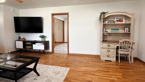 A living room with a flat-screen TV, a wooden coffee table, a bookshelf, and a desk with a chair. - Skyline House - Sunrise Oasis (Searcy)