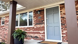 A brick house with a blue door, a porch with brown columns, and a potted plant. - Skyline House - Sunrise Oasis (Searcy)