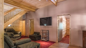 Un intérieur en bois avec un escalier, un fauteuil inclinable en cuir, un téléviseur à écran plat et une bibliothèque.