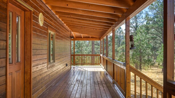 Une cabane en bois dotée d’un porche abrité, de grandes fenêtres et d’une vue sur une forêt.