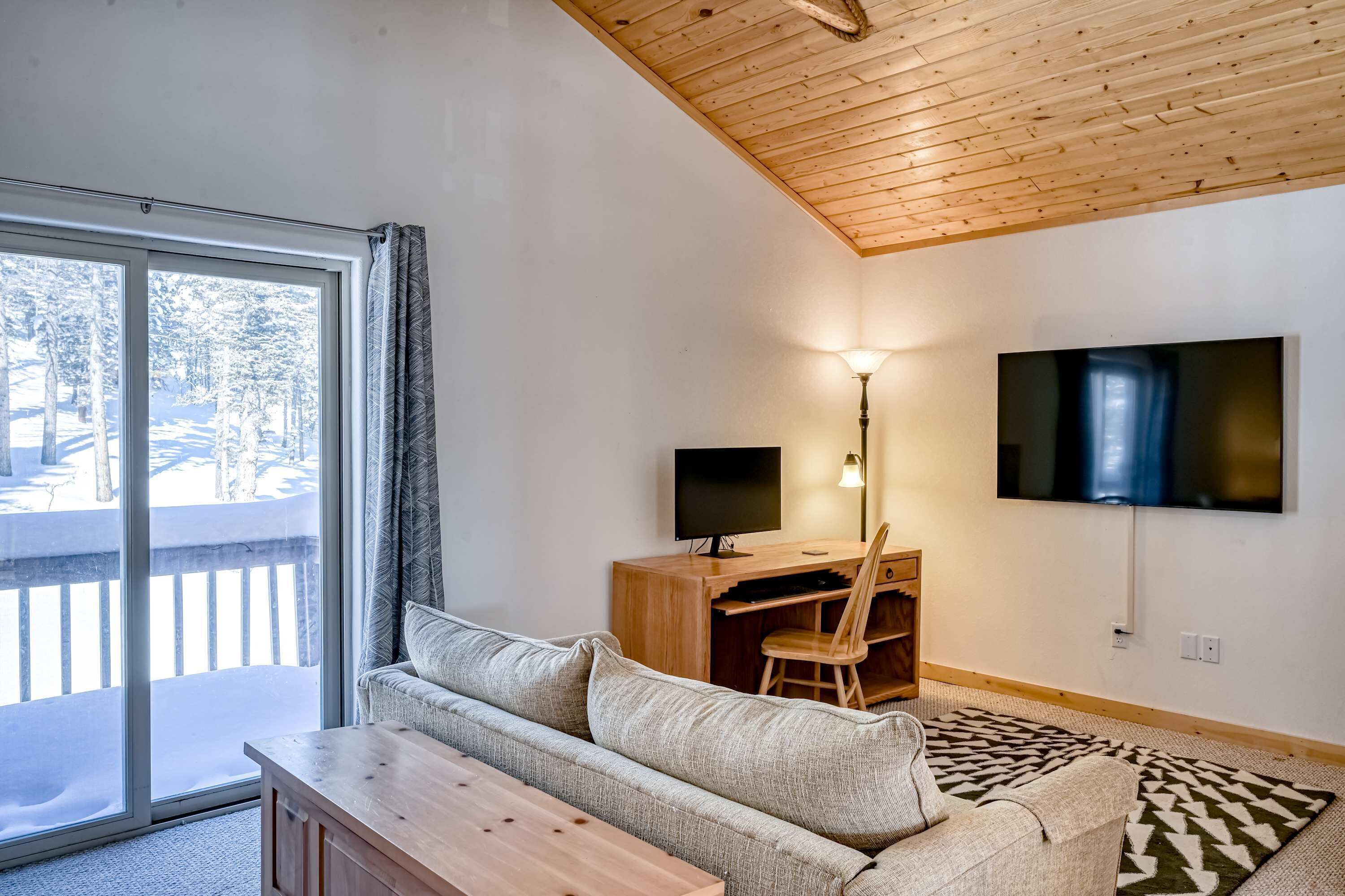 Un salon avec un canapé, un bureau en bois, une télévision et une vue sur un espace extérieur enneigé.
