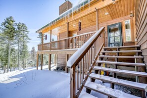 Eine Holzblockhütte mit Balkon und Treppe vor einer verschneiten Landschaft.
