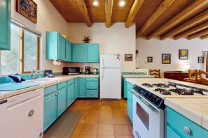 A kitchen with teal cabinets, a white refrigerator, a stove, and wooden ceiling beams.