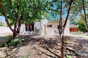A house with a covered outdoor seating area, a small patio, and a garden with trees and shrubs.