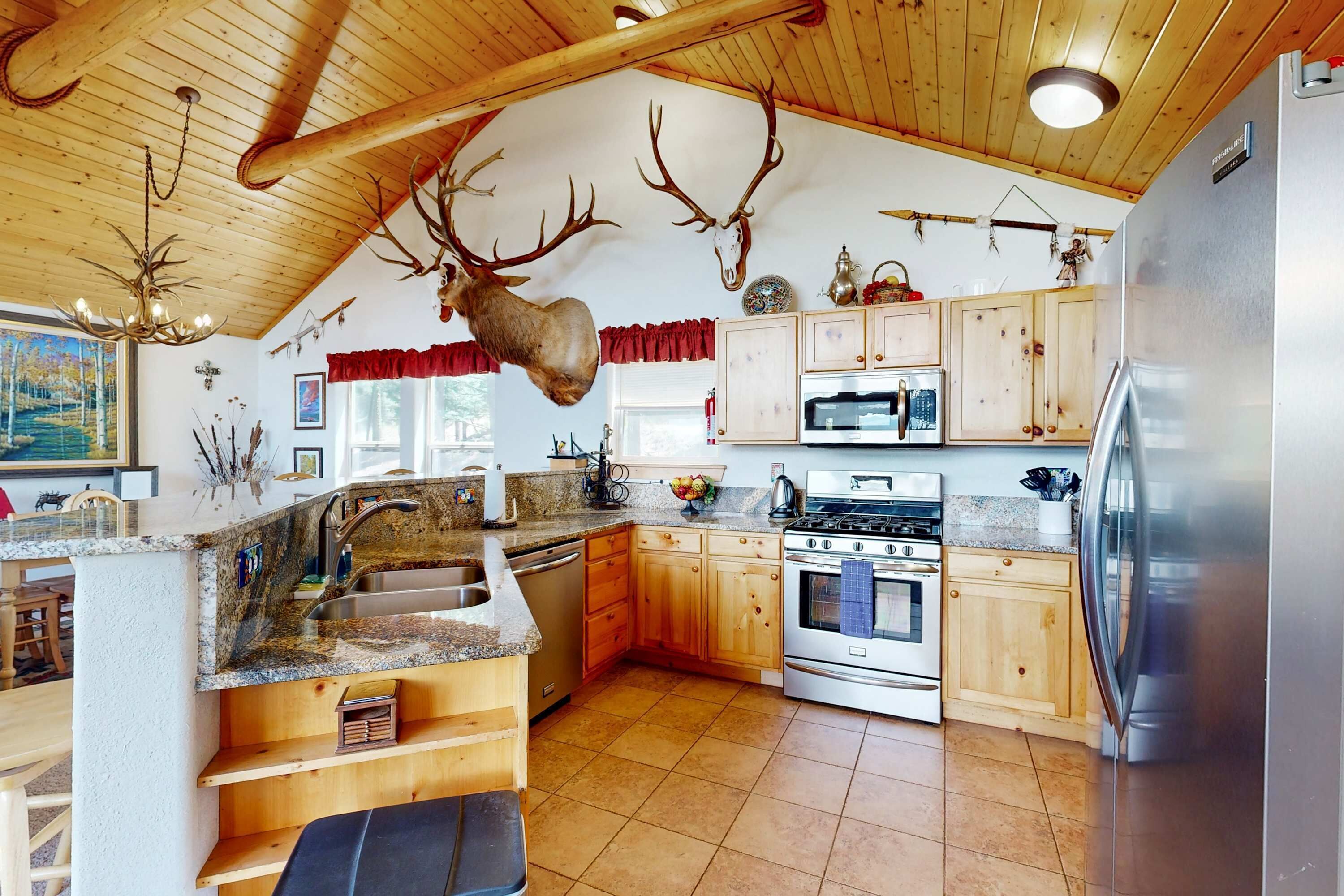 A kitchen with wooden cabinets, a stainless steel refrigerator, and a deer head mounted on the wall.