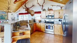 A kitchen with wooden cabinets, a stainless steel refrigerator, and a deer head mounted on the wall. - El Camino Real Retreat - Views, Hot Tub & Pets Ok (Angel Fire)