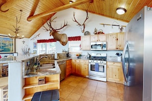 A kitchen with wooden cabinets, a stainless steel refrigerator, and a deer head mounted on the wall. - El Camino Real Retreat - Views, Hot Tub & Pets Ok (Angel Fire)