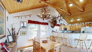 A wooden interior with a dining table, chairs, a chandelier, and a mounted deer head. - El Camino Real Retreat - Views, Hot Tub & Pets Ok (Angel Fire)