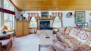 A cozy living room with a fireplace, wooden ceiling, and a sofa with patterned cushions. - El Camino Real Retreat - Views, Hot Tub & Pets Ok (Angel Fire)