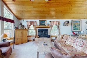 A cozy living room with a fireplace, wooden ceiling, and a sofa with patterned cushions. - El Camino Real Retreat - Views, Hot Tub & Pets Ok (Angel Fire)