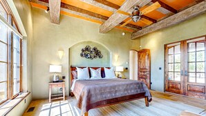 A bedroom with a large bed, wooden ceiling beams, a decorative wall piece, and a large window. - Windy Acres Retreat - Patio, Outdoor Kitchen, Gym (Santa Fe)