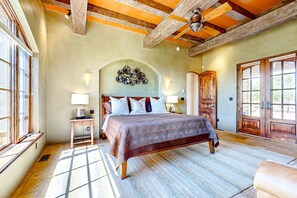 A bedroom with a large bed, wooden ceiling beams, a decorative wall piece, and a large window. - Windy Acres Retreat - Patio, Outdoor Kitchen, Gym (Santa Fe)