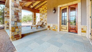 A covered patio with stone walls, a wooden door, and a bench. - Windy Acres Retreat - Patio, Outdoor Kitchen, Gym (Santa Fe)