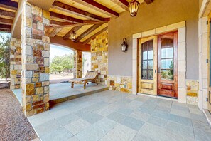 A covered patio with stone walls, a wooden door, and a bench. - Windy Acres Retreat - Patio, Outdoor Kitchen, Gym (Santa Fe)