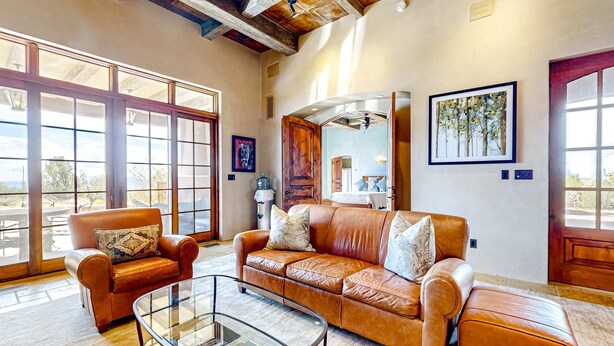 A spacious living room with leather furniture, large windows, and a high ceiling. - Windy Acres Retreat - Patio, Outdoor Kitchen, Gym (Santa Fe)