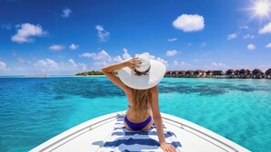 Une personne se trouve sur un bateau, d’où elle a une vue dégagée sur une eau turquoise et sur des bungalows sur pilotis en arrière-plan.