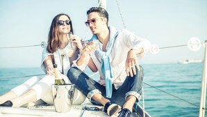 Deux personnes se trouvent sur un bateau, tenant des verres, avec une bouteille et un récipient en métal sur le pont.