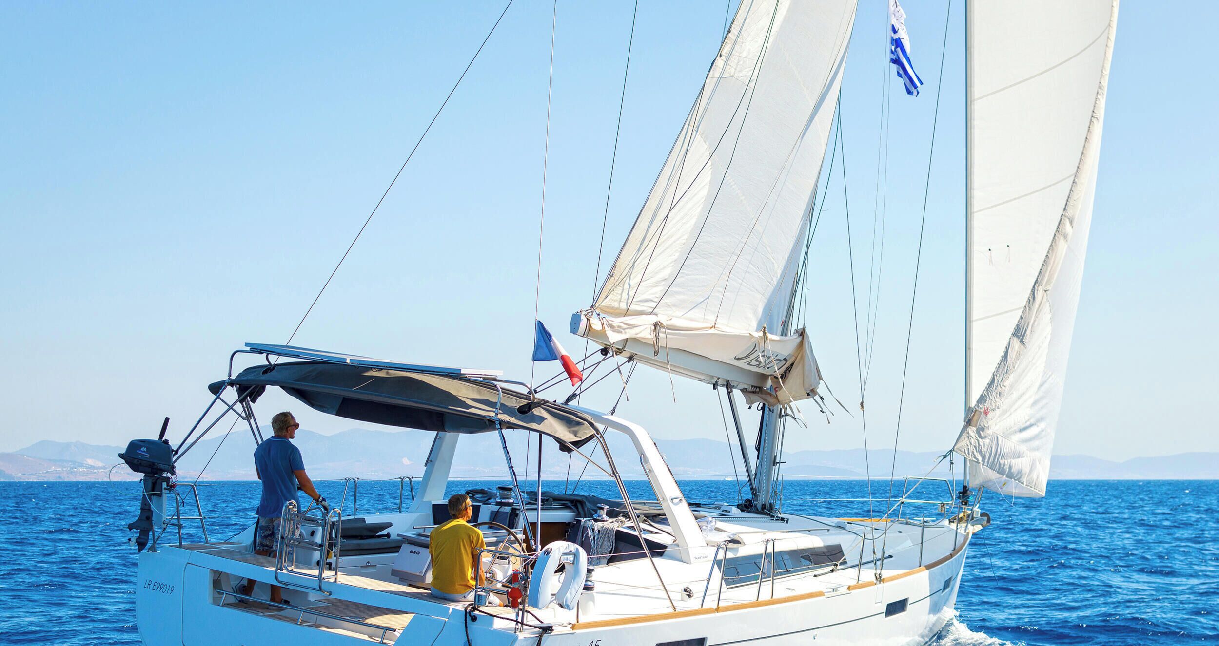 Eine Segelyacht mit Kabine, eine Person am Steuer und eine weitere Person auf dem Deck.