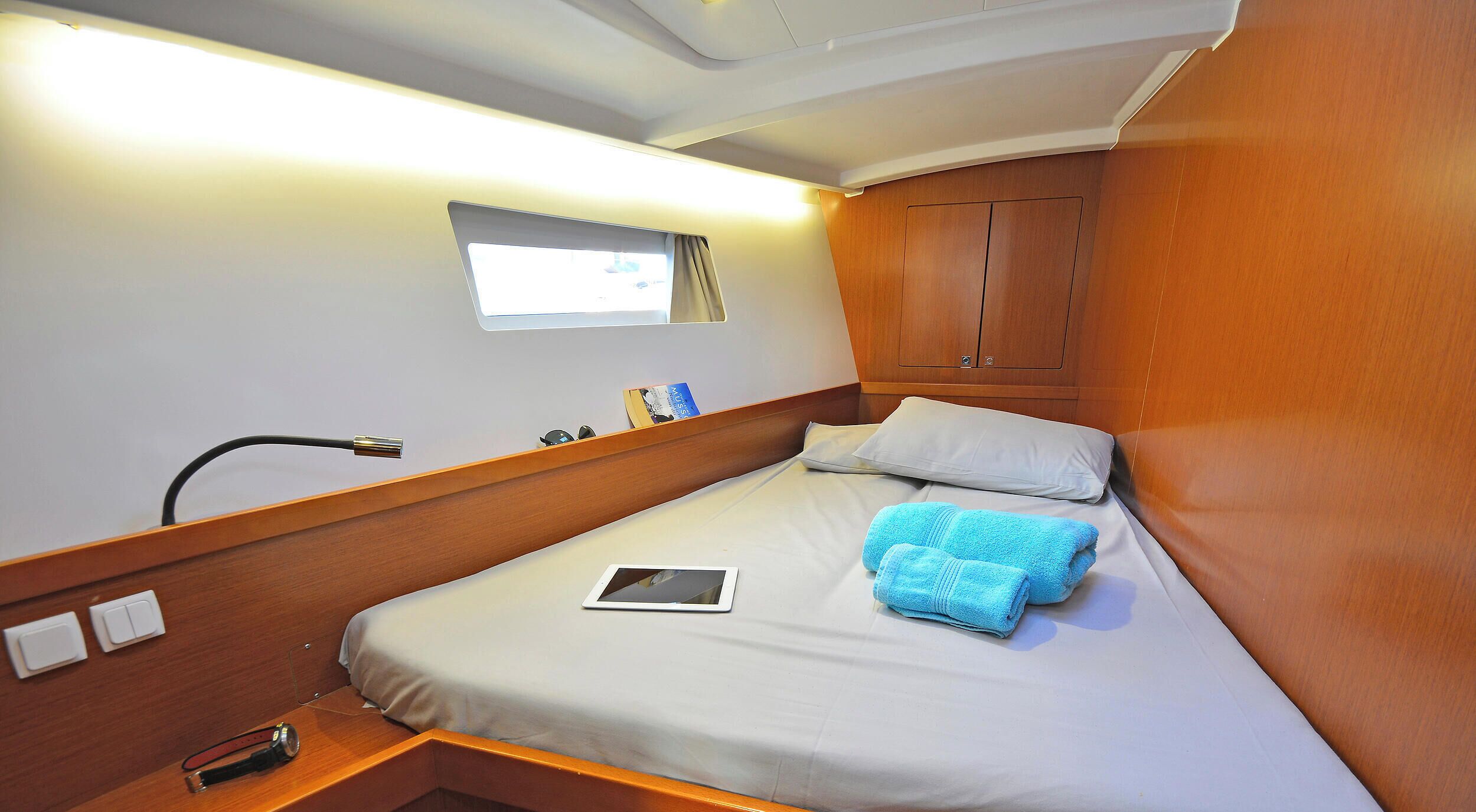 Un lit simple avec un matelas blanc, une serviette bleue, une tablette et une fenêtre avec des rideaux.