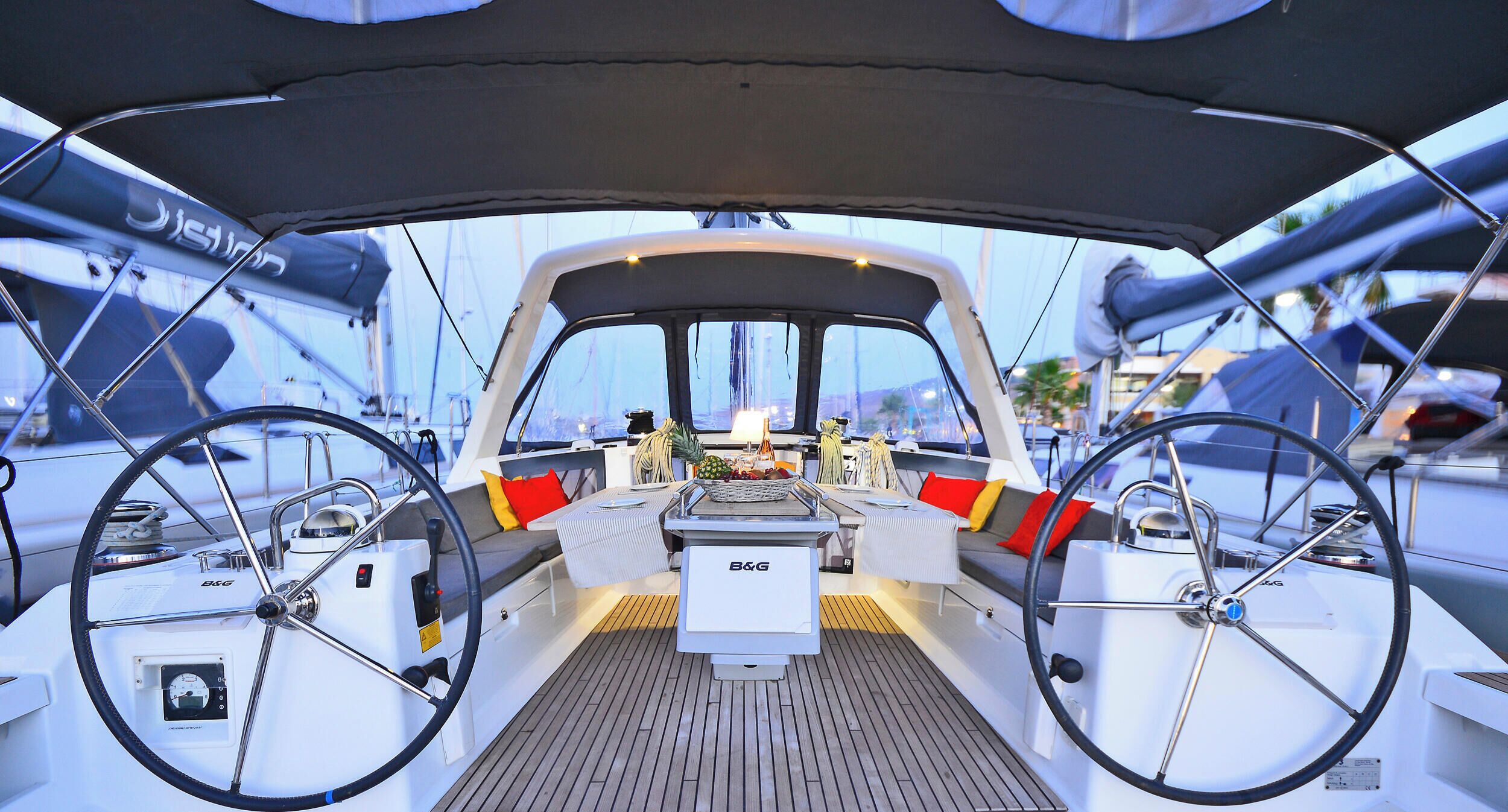A boat's deck with a steering wheel, B&G control panel, and seating area.