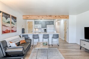 Ein modernes Wohnzimmer mit Sofa, Couchtisch und einer Küchenzeile mit Barhocker.