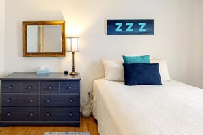Ein Schlafzimmer mit Bett, Kommode, Spiegel, Wanduhr und einem an der Wand befestigten Schild.