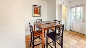 A dining area with a wooden table and chairs, a framed abstract painting on the wall, and a door leading to another room. - Kathryn Place Casita - Walk to Downtown & Railyard (Santa Fe)
