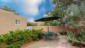 A patio with a table and chairs, surrounded by greenery and a building. - Kathryn Place Casita - Walk to Downtown & Railyard (Santa Fe)