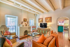 A living room with a sofa, armchairs, a coffee table, a television, and a kitchen visible through an archway. - Casa De Muneco - Adobe Charm, Steps from Canyon Rd (Santa Fe)