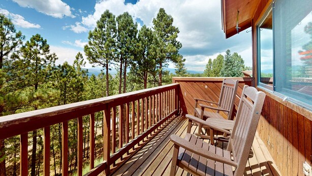 A wooden deck with chairs and a table, overlooking a forested area. - The Lift C2 - Walk to Lifts & Town, Mountain Views (Angel Fire)