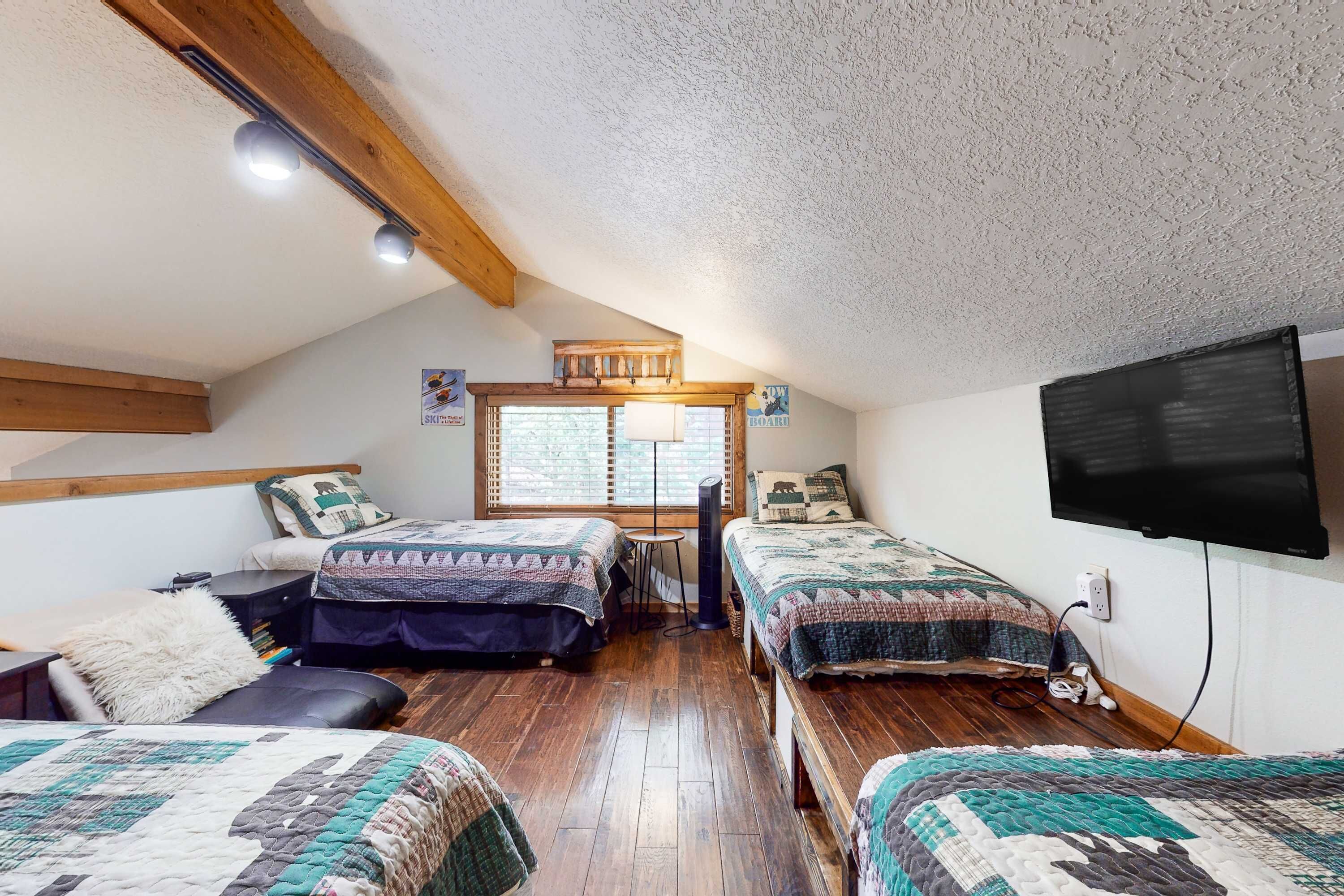 A cozy attic bedroom with two beds, a wooden ceiling, a TV, and a window.