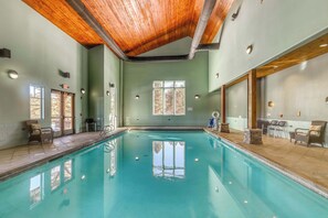 An indoor swimming pool with wooden ceiling beams, a tiled floor, and a view of the outdoors through windows. - Angelica's Sorrento Home - Hike & Monte Verde Lake (Angel Fire)