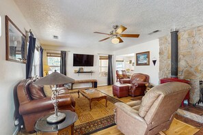 A living room with leather sofas, a coffee table, a TV, and a stone fireplace. - Angelica's Sorrento Home - Hike & Monte Verde Lake (Angel Fire)
