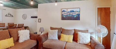 Sala de estar com dois sofás marrons, teto de madeira, relógio de parede, um quadro e um ventilador.