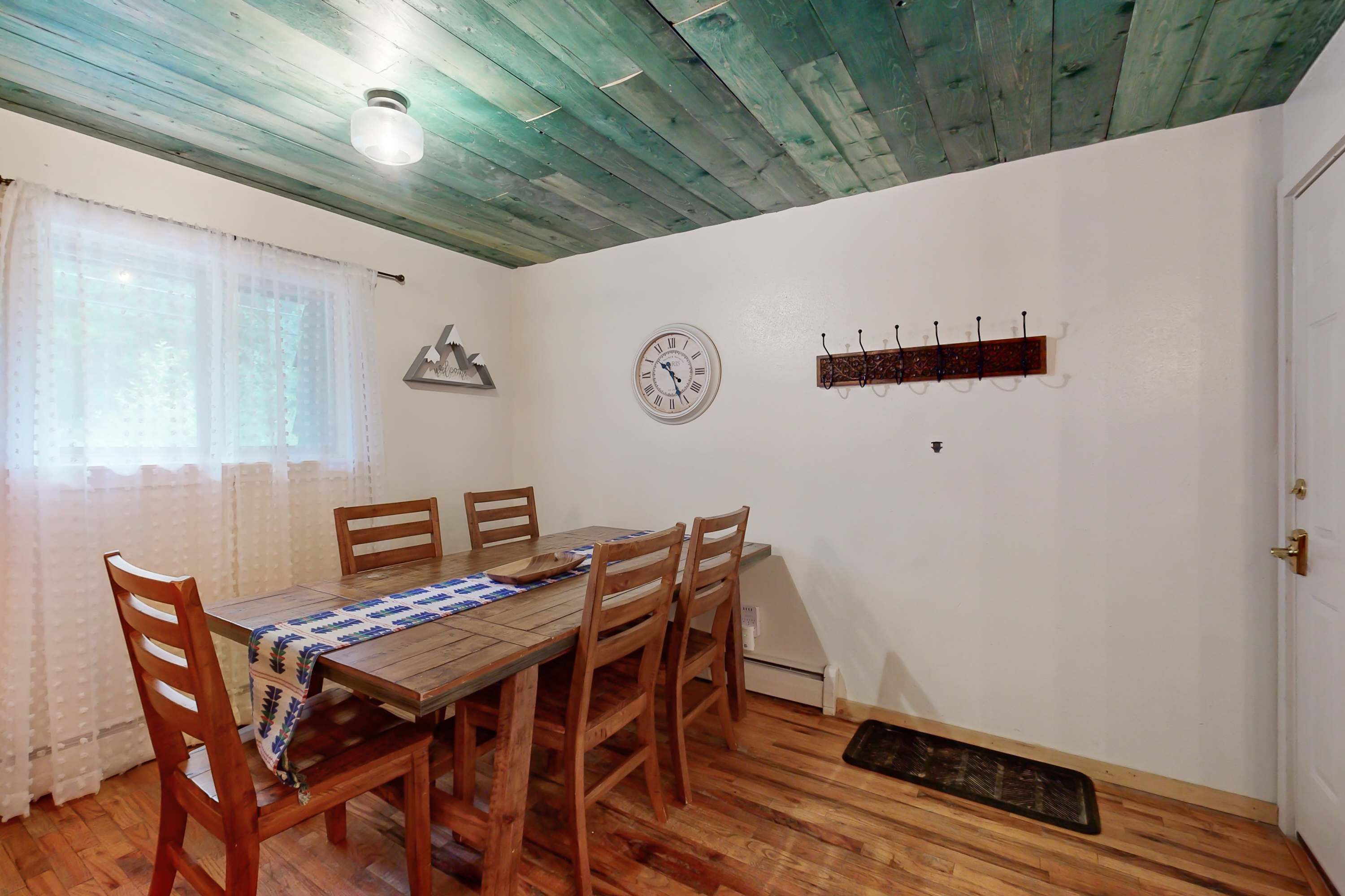 Comedor con mesa y sillas de madera, un reloj en la pared y techo con vigas a la vista.