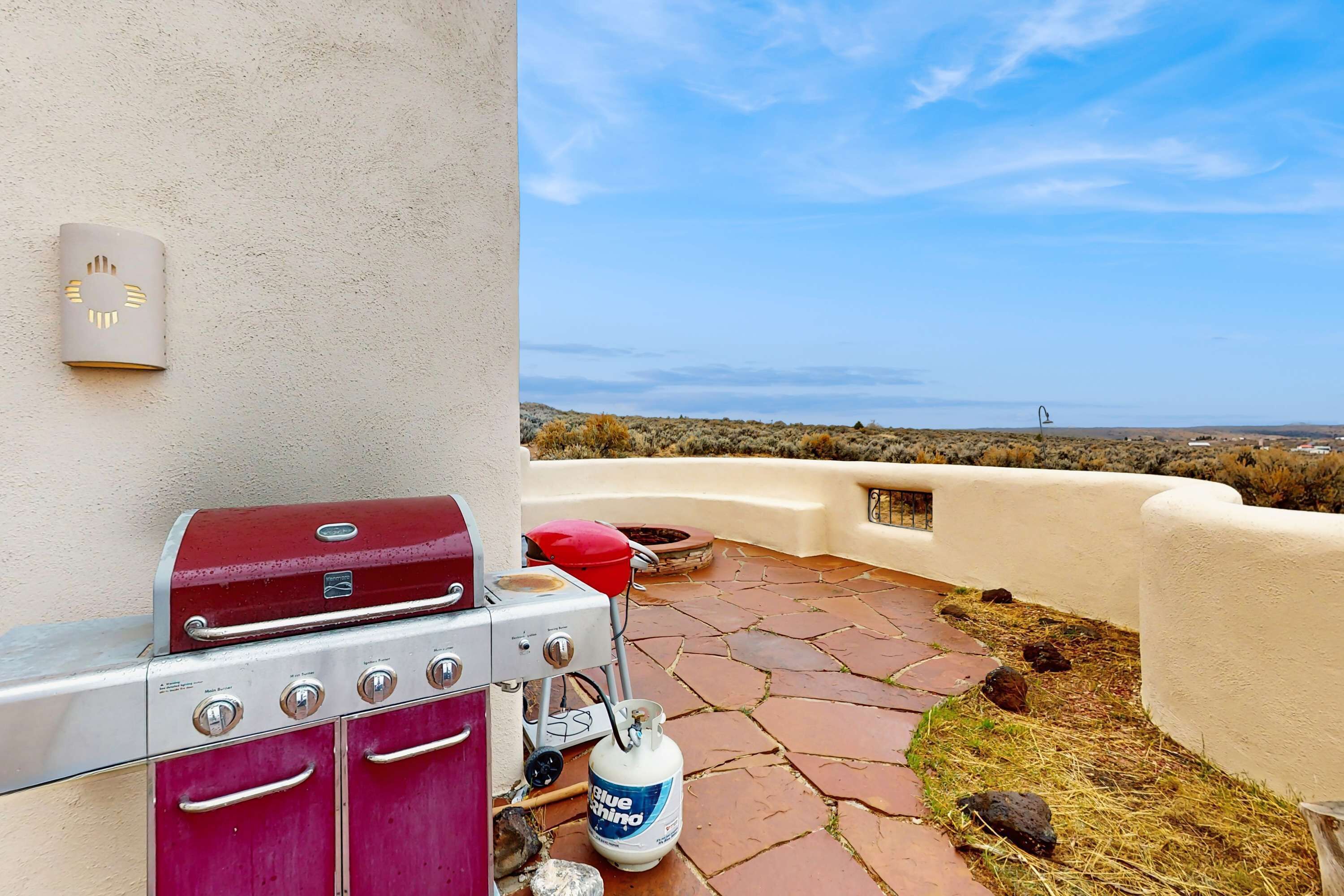 A barbecue grill and gas tank on a patio with a view of the ocean.